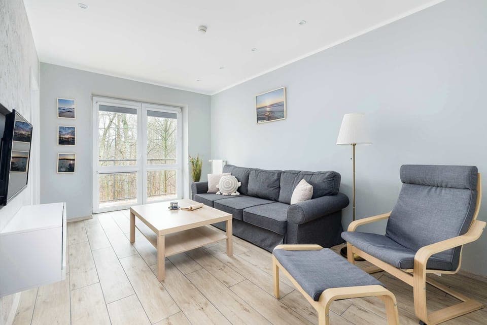A cozy living room with comfortable armchair and sofa, and a coffee table, with natural light streaming in.