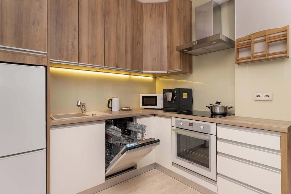 Modern, fully equipped kitchen in light tones with wooden cabinet fronts, oven, dishwasher and microwave. A brilliantly designed, functional kitchen interior.