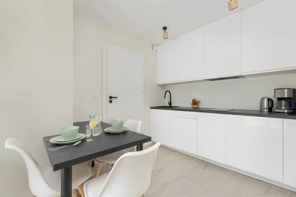 A sleek dining area connected to the kitchen, featuring white cabinetry. The setup is minimalistic yet functional.