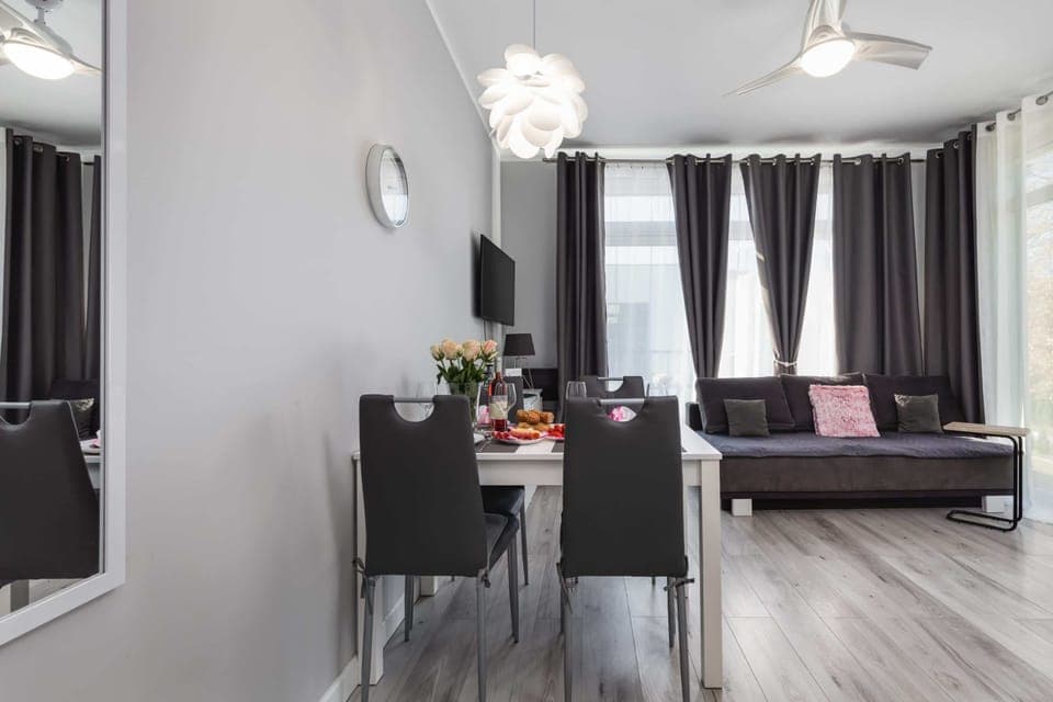 A stylish dining and living area featuring a dining table set for four, a cozy sofa, and large windows for natural light.
