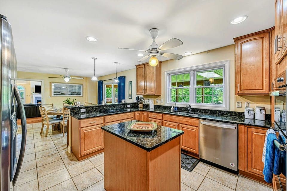 Kitchen - Maple cabinets with dark granite countertops, center island, ceiling fan, and open sightline to the dining area.