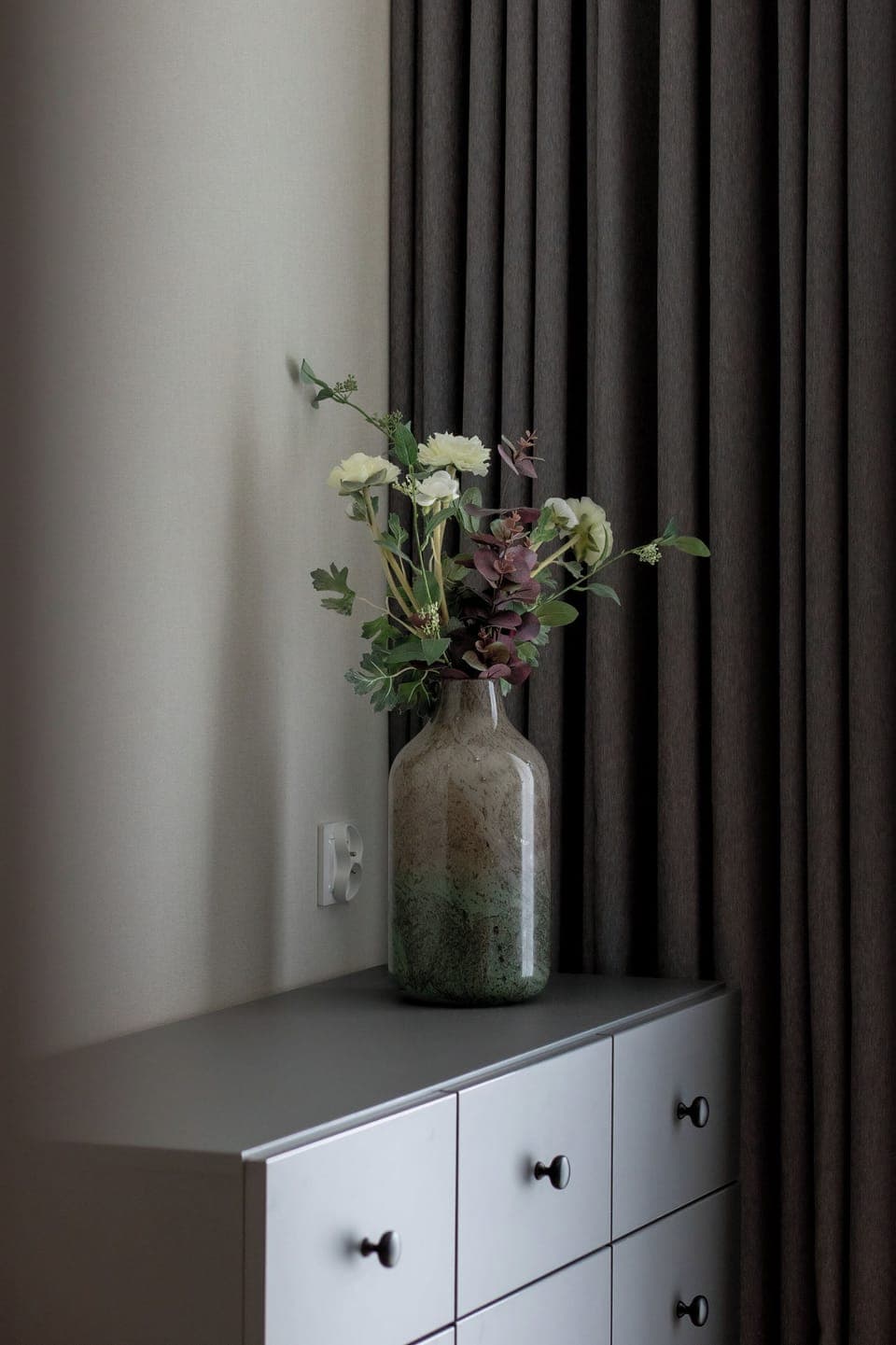 A decorative corner with a vase of flowers on a white drawer unit. Simple and elegant, it adds softness to the studio.