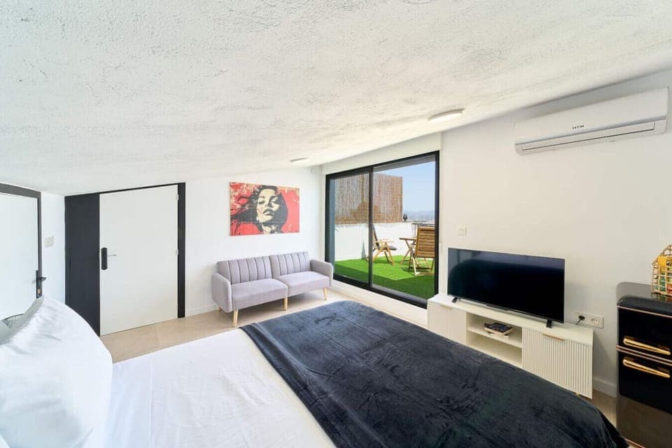 Double bed (135cm x 200cm), sofa bed which comfortably sleeps one adult, TV Stand with TV, fridge, and view of the terrace with outdoor furniture.