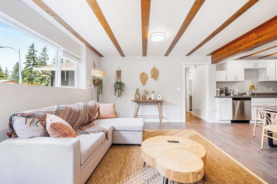 Modern open-concept living space​ featuring an L-shaped dove gray sofa with vibrant throw blankets and blush pillows, centered around a unique live-edge coffee table with visible wood grain.