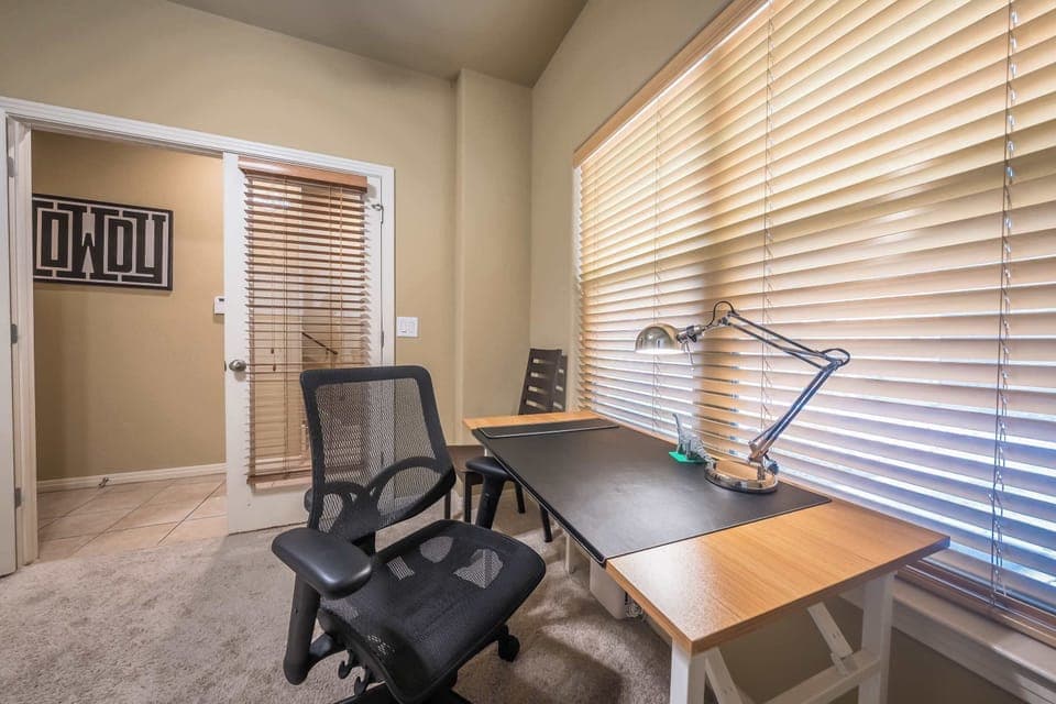 desk with lamp and desk chair with 2 chairs on either side on the desk with entrance to office 