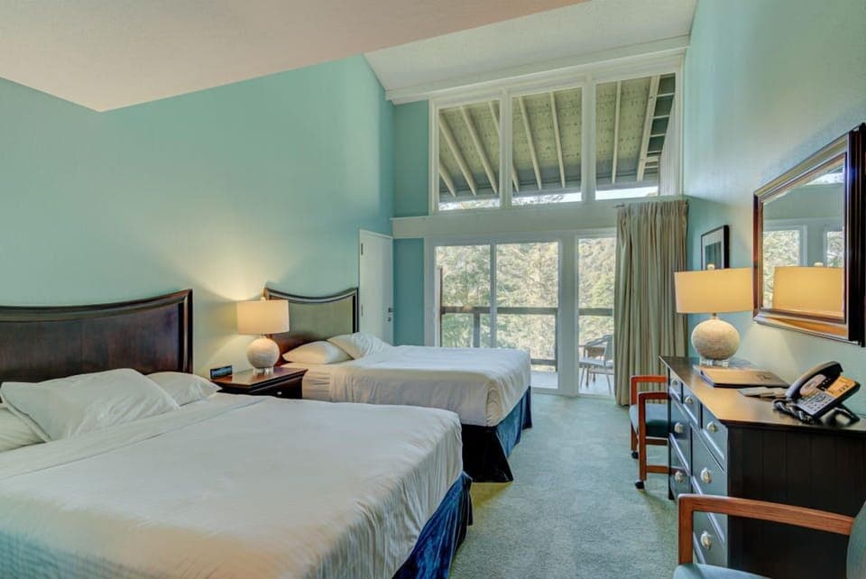 This cozy Forest View 2 Queen Bedroom features two inviting queen beds alongside a spacious sitting area, all bathed in natural light from the large balcony that offers serene forest views.