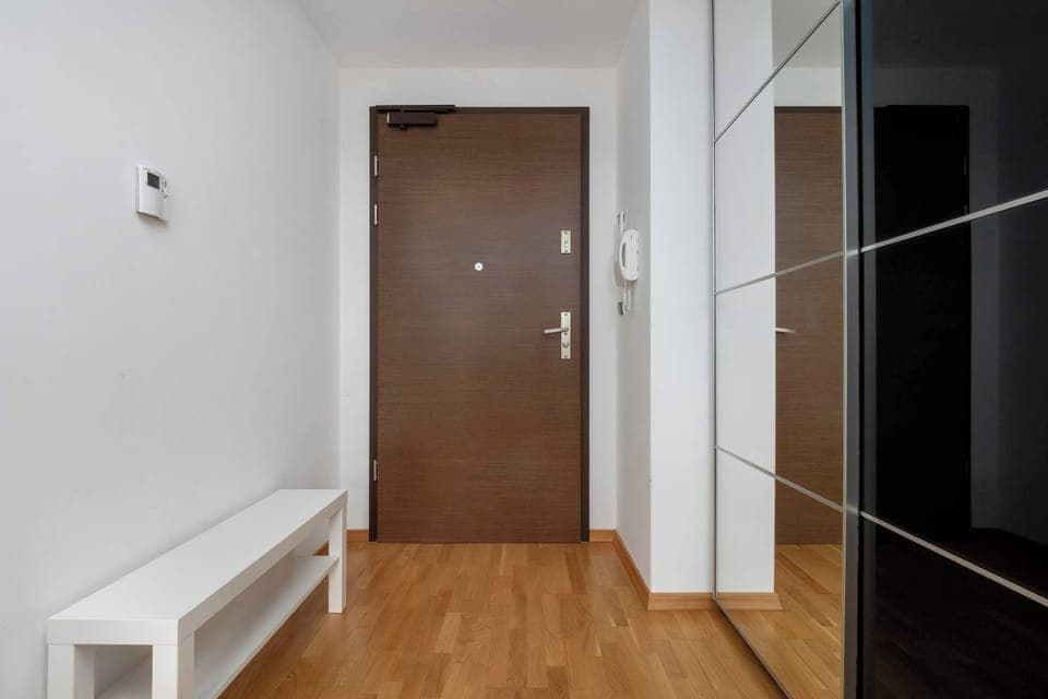 An apartment entrance with a wooden door and hallway. The area is bright and simple, providing a welcoming first impression.