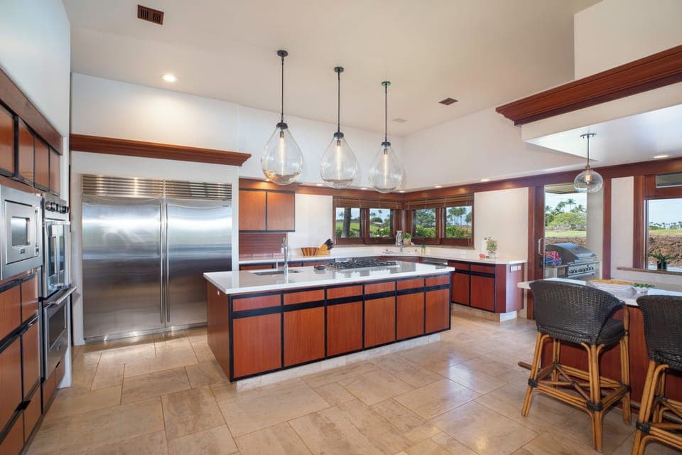 Your gourmet kitchen invites culinary adventures with gleaming stainless appliances, spacious island, and warm wood cabinetry overlooking tropical views.