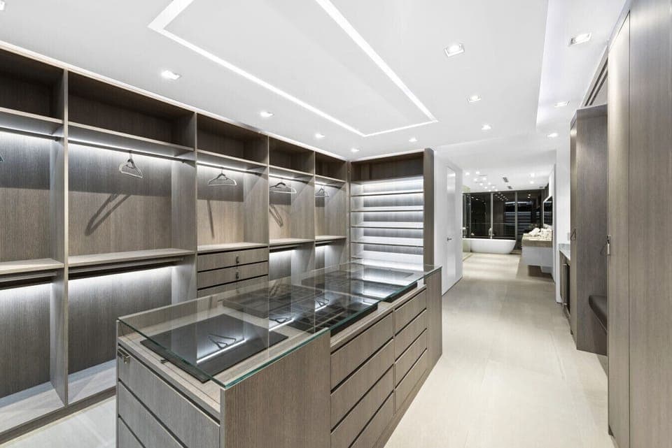 Luxury dressing room featuring center display island, illuminated storage, and sleek cabinetry