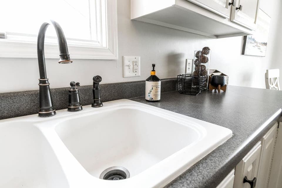 A deep double sink with a modern bronze faucet, stylish soap dispenser, and sleek countertops for all your washing and prepping needs.