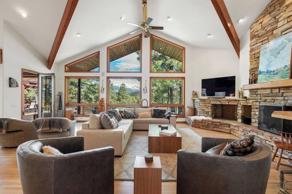 The heart of the home — a bright and inviting great room with soaring ceilings, a cozy stone fireplace, and large windows framing beautiful mountain views. A perfect space to relax, share stories, or unwind after a day exploring Durango.