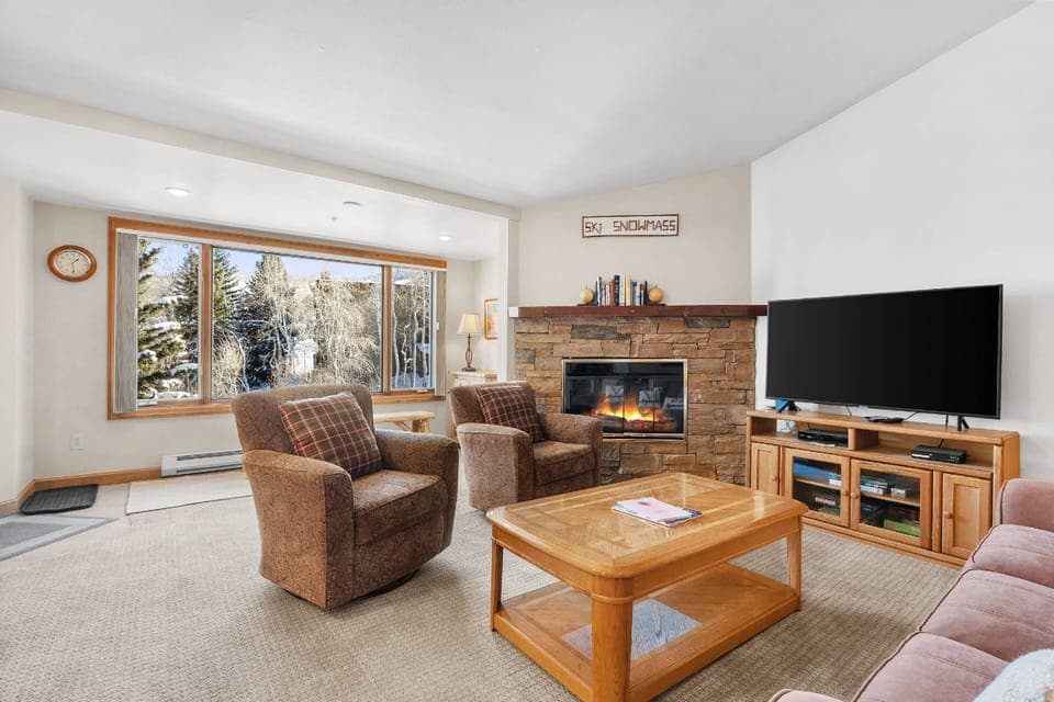 Cozy living room with stone gas fireplace, comfortable seating, and large windows showcasing beautiful views.