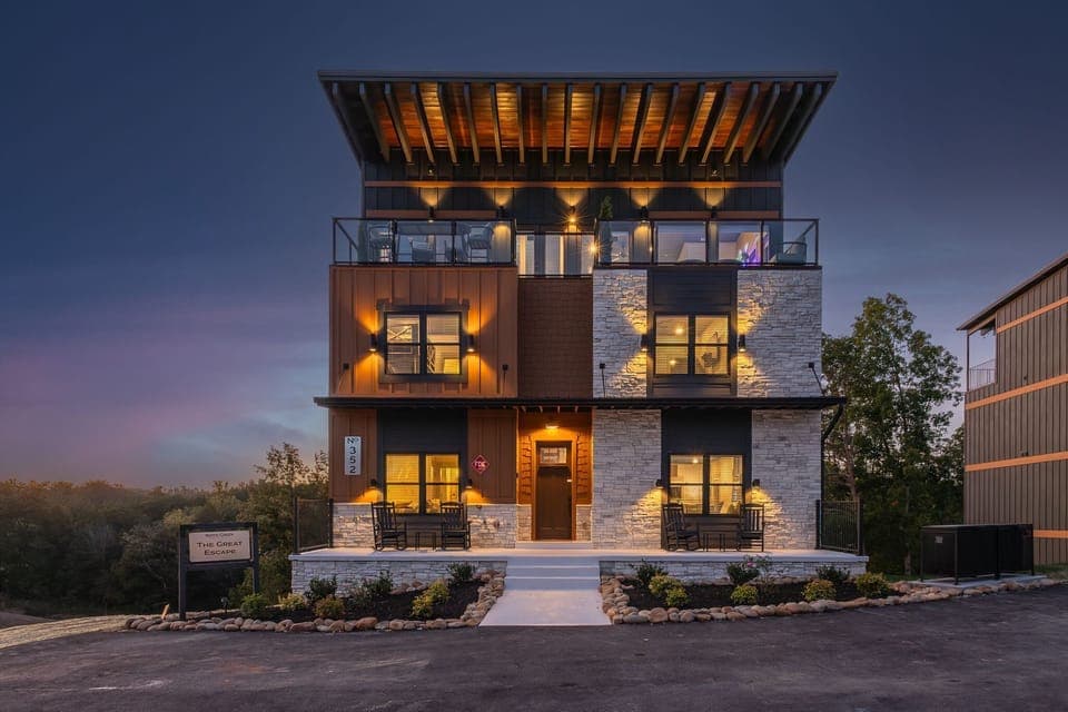 Modern three-story home with illuminated stone and wood exterior and spacious balconies.
