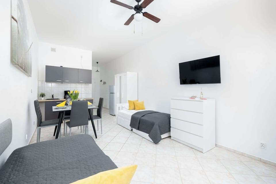 Bright and modern open-plan living area with a comfortable single beds, wall-mounted TV, and a cozy dining corner in soft neutral tones.