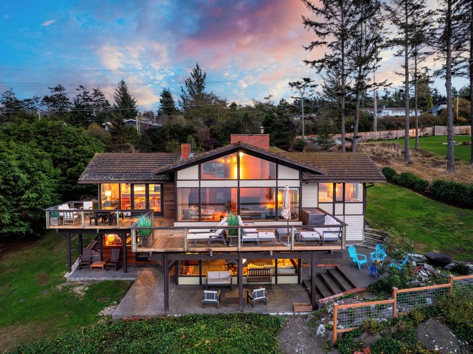 Sunset view of the main house with glowing interior lights and deck seating.