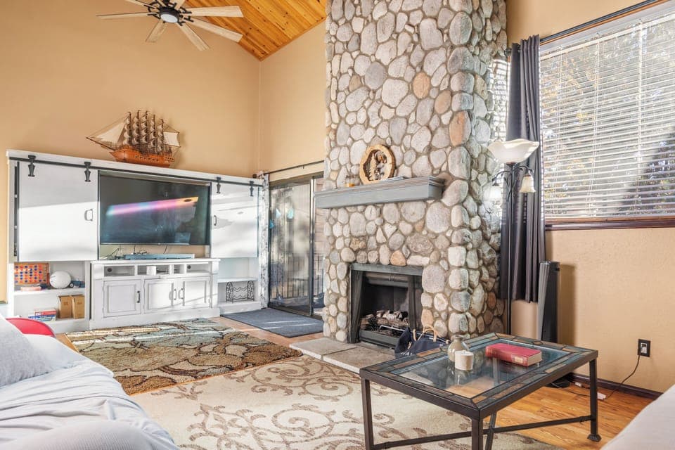 Living area with a stone fireplace, TV and large window for a natural light.