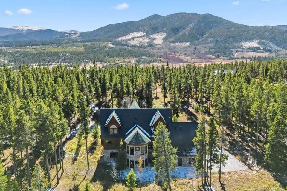 Mountain lodge nestled among towering pines with dramatic peaks creating a stunning backdrop.