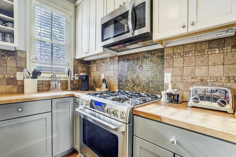 This section of the kitchen features a gas range, built-in microwave, and ample counter space for cooking with ease. Warm tile accents and natural light keep the space feeling bright and inviting.