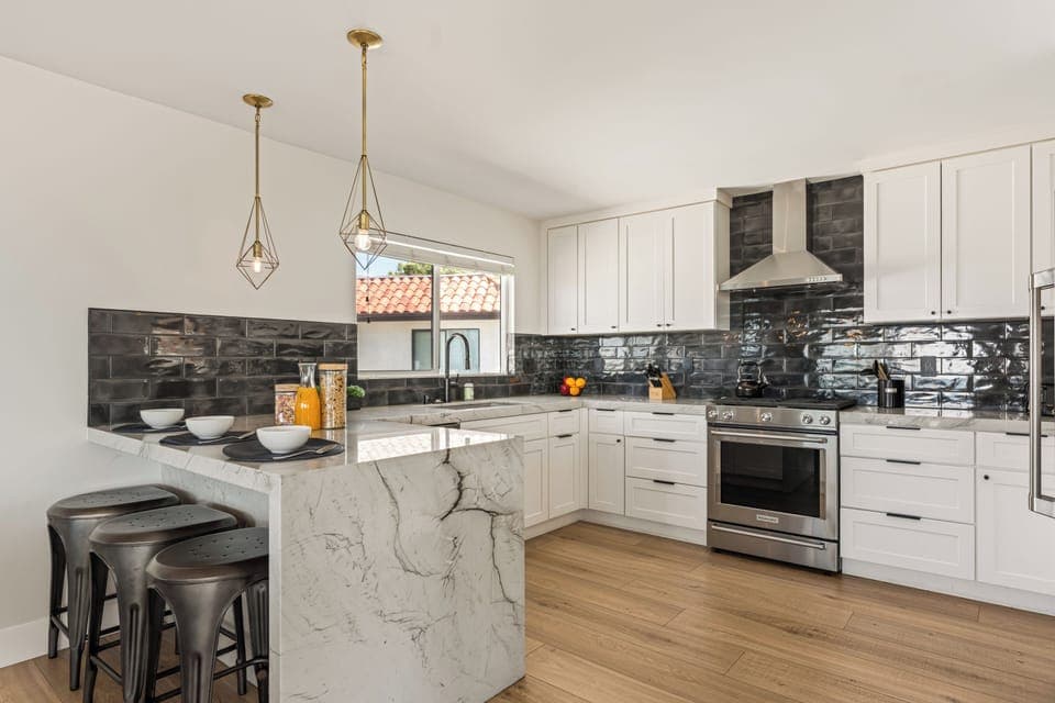 Sleek modern kitchen with marble waterfall island, stainless steel appliances, and chic black tile backsplash—perfect for gathering and entertaining.