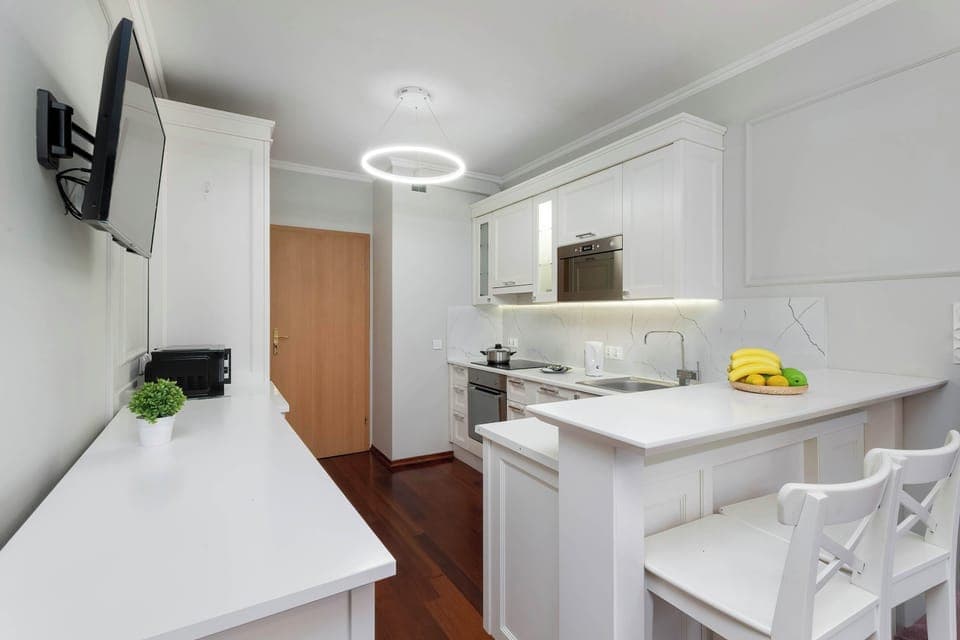 An open-plan kitchen and living area with white cabinetry and a round dining table. Comfortable seating and wooden floors create a warm ambiance.