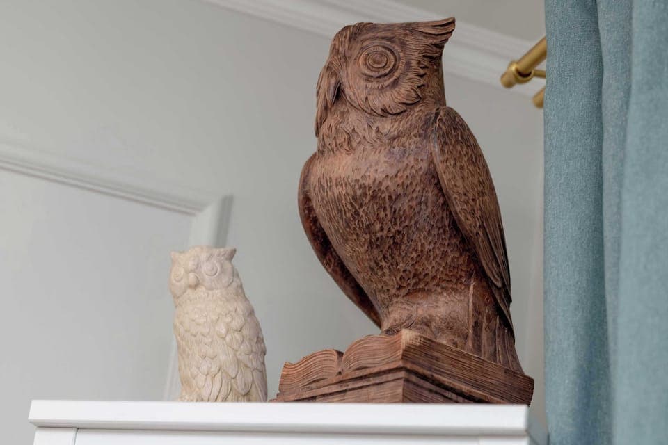 A decorative wooden owl sculpture on a shelf, accompanied by a smaller decorative item. Adds character and artistic detail to the space.