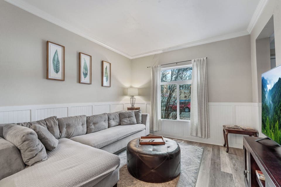 Sink into the plush sectional sofa in your cozy living space, where natural light streams through large windows and thoughtful botanical artwork creates a serene atmosphere.