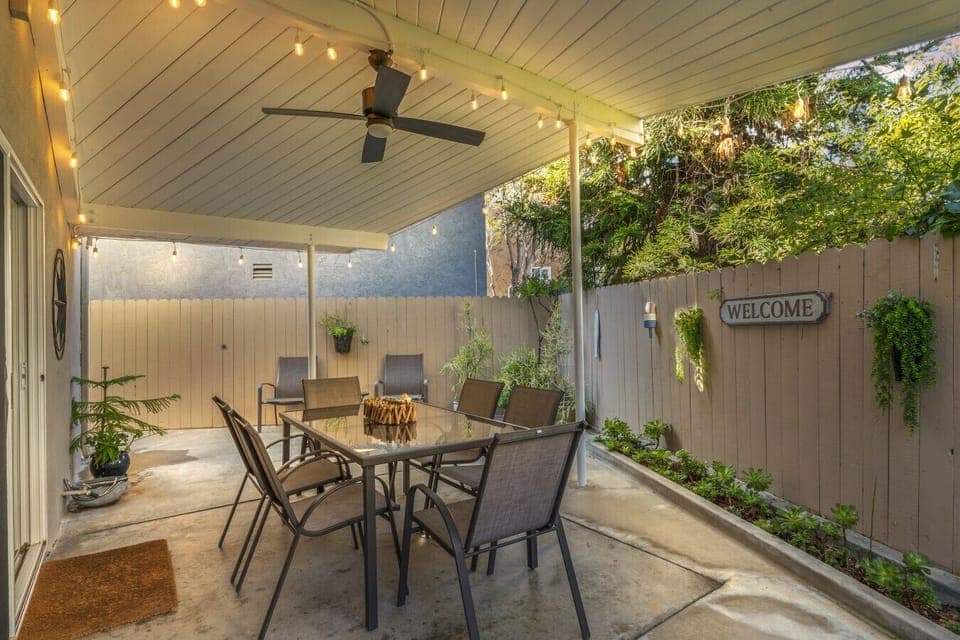 Enjoy this inviting covered patio featuring outdoor dining, warm lighting, and lush greenery.