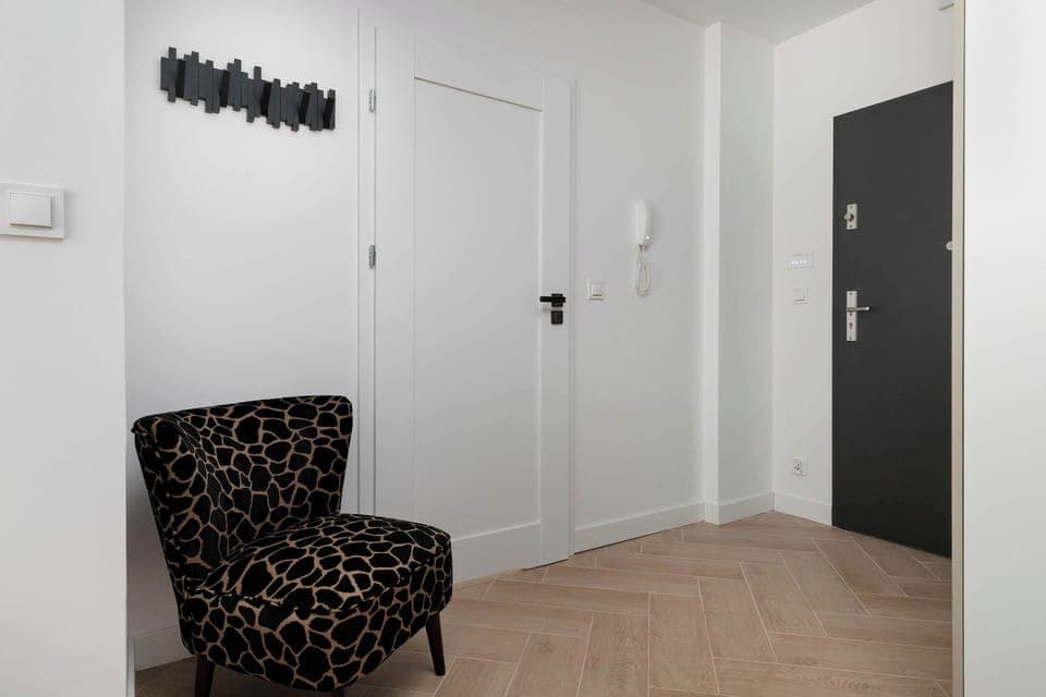 Hallway view with a patterned chair and the main entrance door, providing a welcoming entry space.