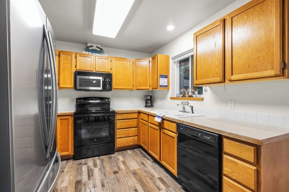 Kitchen with light wood cabinets, black appliances, and wood-look flooring.