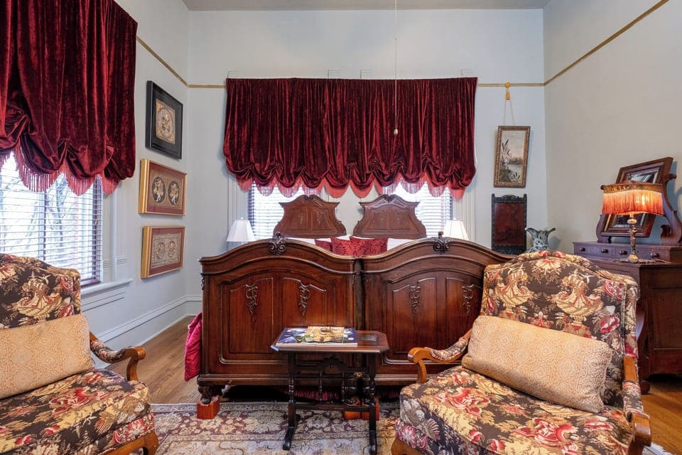 Primary sleeping area with tall windows, custom drapery, and classic Victorian charm.