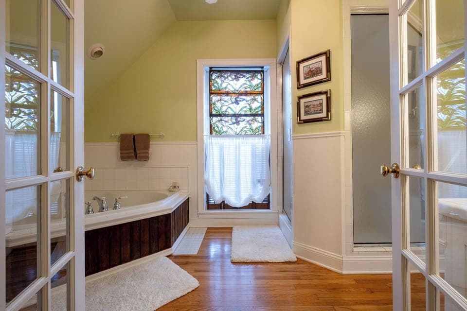 Spa bathroom entry featuring a soaking tub set beneath a stained-glass window as well as walk-in shower.
