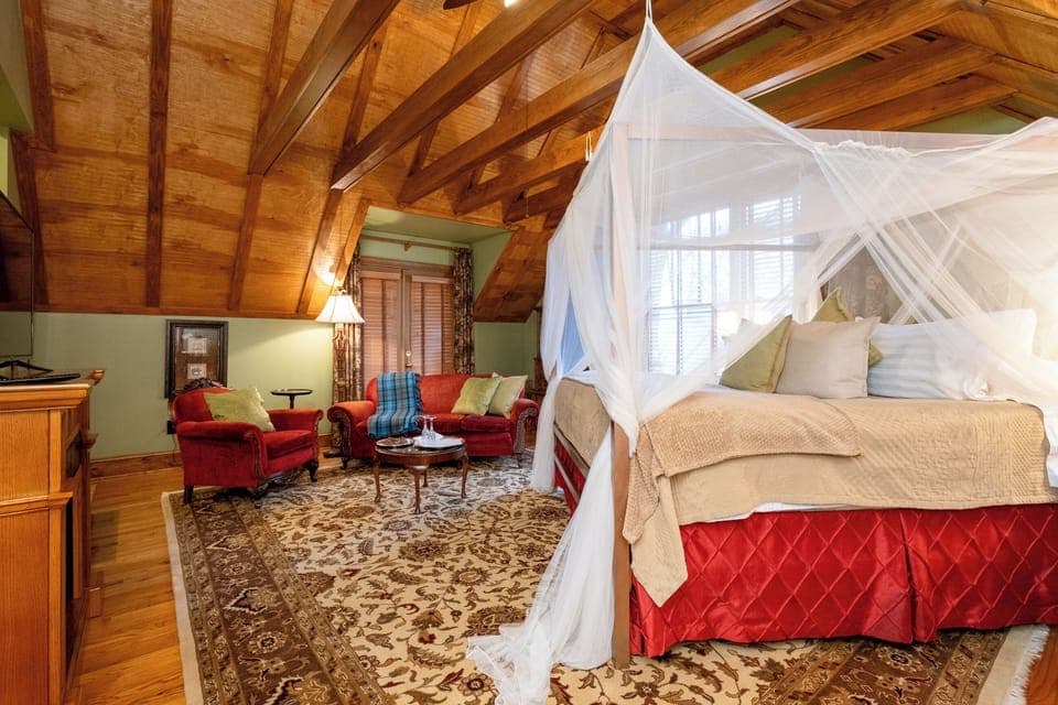 The Hemingway Spa Suite bedroom with exposed wood-beam ceiling, canopy bed, and intimate sitting area.