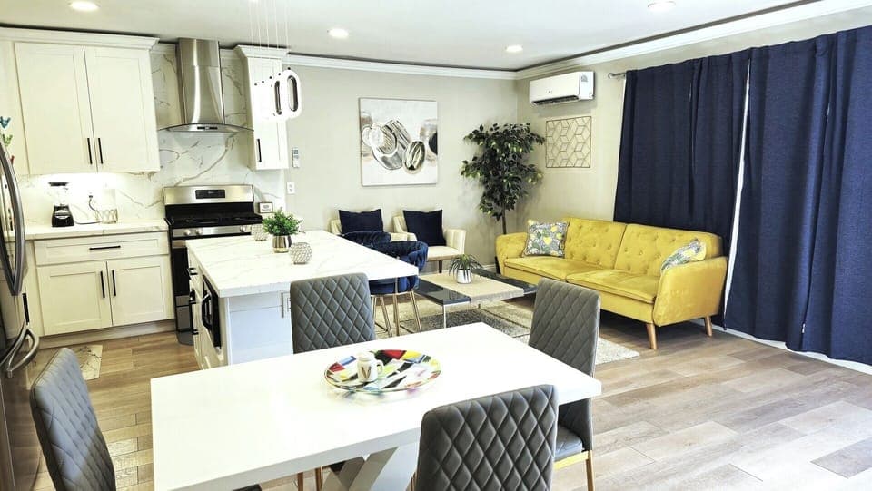 Open‑plan living and dining area with modern kitchen, yellow sofa, dining table, navy curtains, wooden flooring, and contemporary decor.
