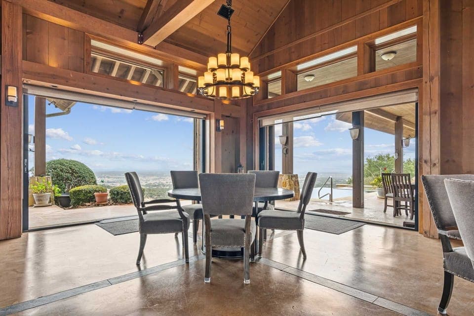This magnificent space features dramatic post-and-beam construction with wood-plank ceiling and a spectacular tiered chandelier. Massive sliding glass panels open to reveal a massive patio, infinity pool, and a breathtaking vista of the rolling hills