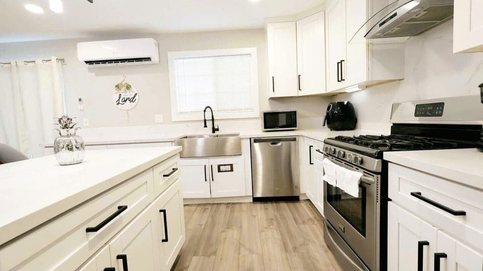 Modern, fully equipped kitchen featuring white shaker cabinets, stainless steel gas range with chimney hood, and sleek countertops. Bright, minimalist design with ample storage and counter space.