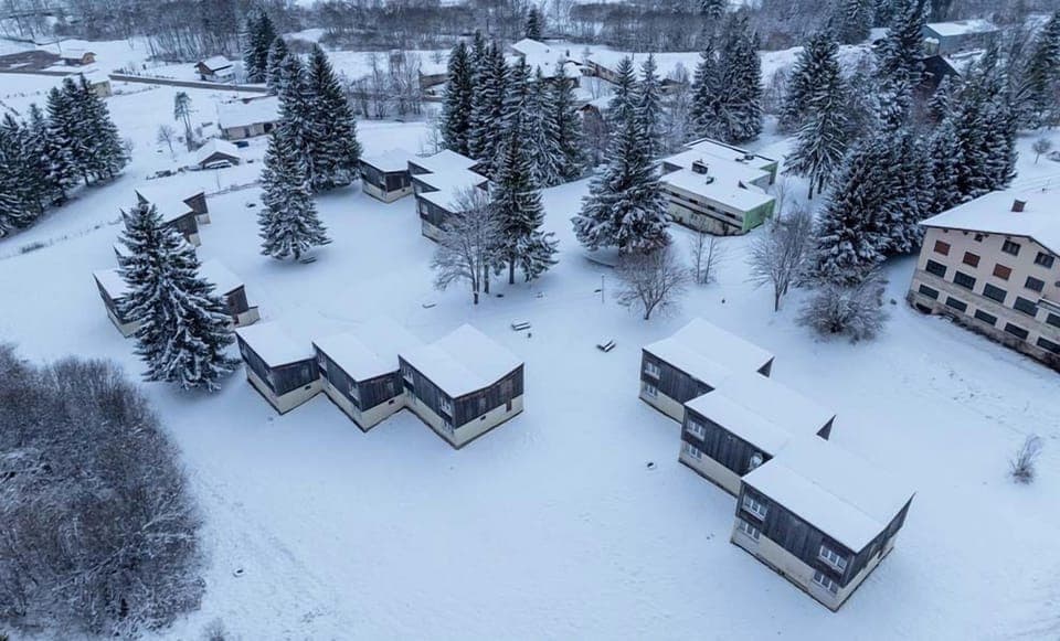 Aerial view of Résidence Les Monts Jura, where cozy lodges are blanketed in soft snow amidst tall evergreen trees.