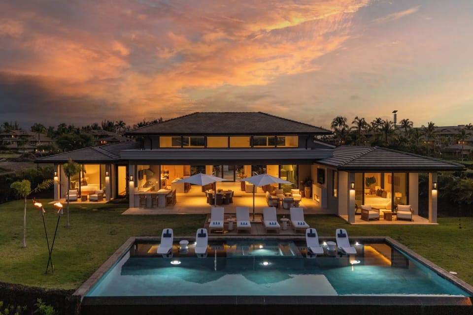 Luxurious villa surrounded by tropical palms, featuring a stunning swimming pool and outdoor dining areas under dramatic sunset skies.