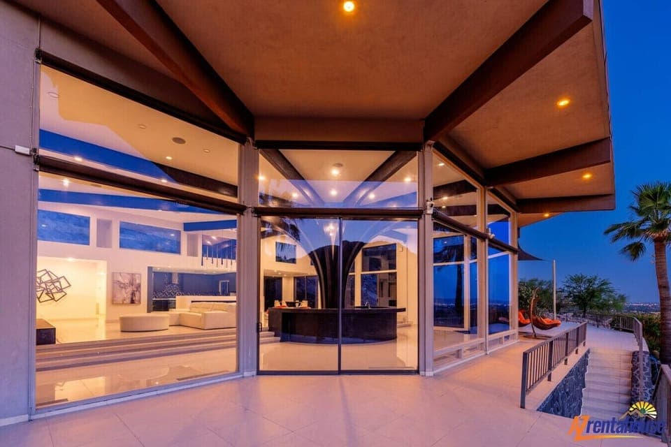 Modern luxury home with stunning glass walls and open architecture overlooking city lights at dusk.
