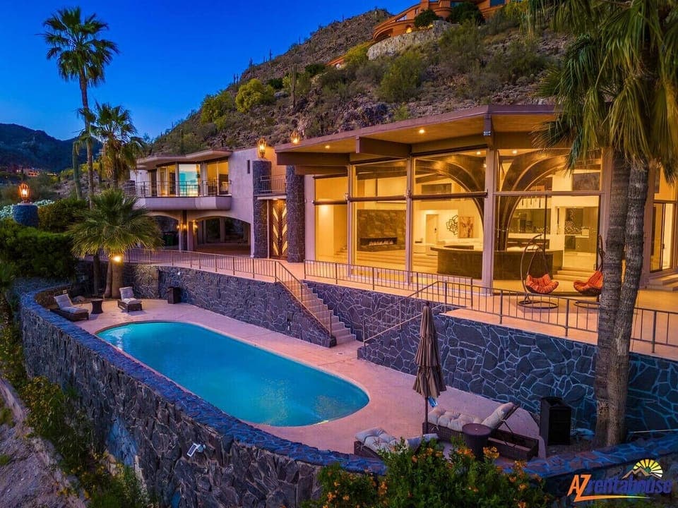 Stunning hillside villa features contemporary architecture with palm trees, private pool, and illuminated terraces set against dramatic mountain backdrop.