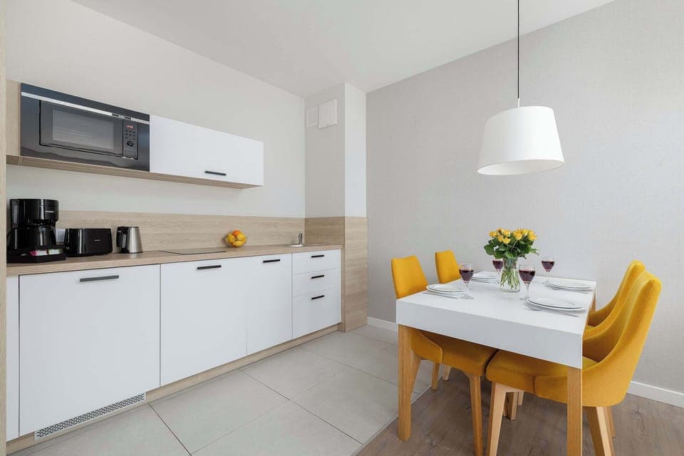 A compact kitchen and dining corner with white cabinetry, integrated appliances, and a small table set for two.