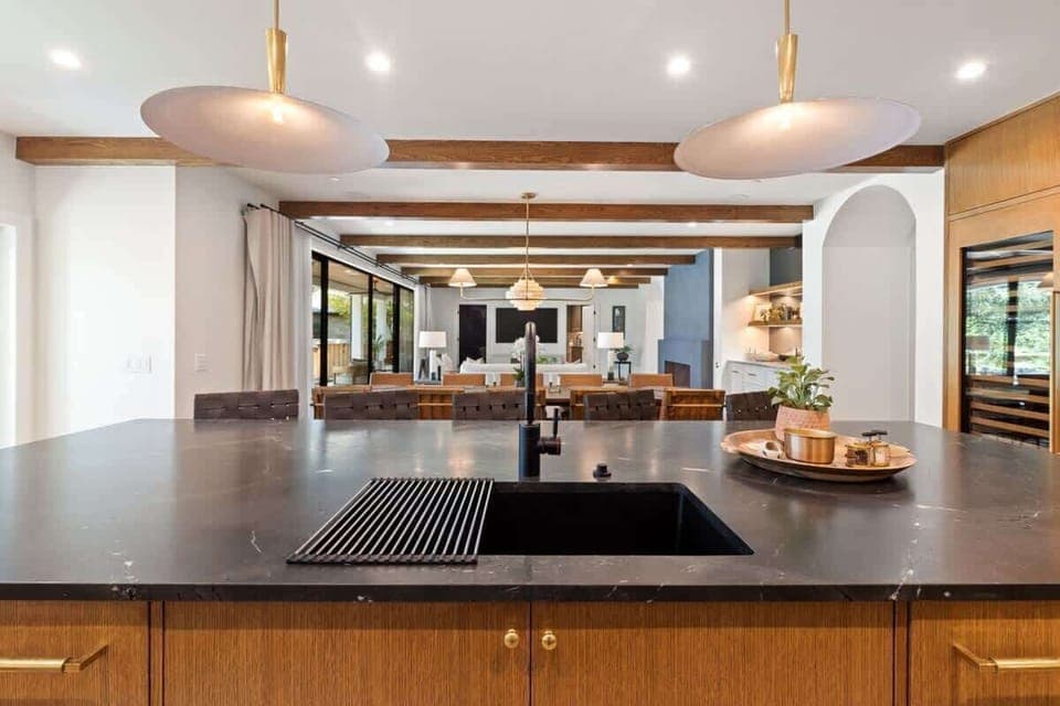 This chef’s kitchen boasts Wolf appliances, dual dishwashers, twin Sub-Zero fridge and freezer, warming drawer, wine fridge, and a sleek island with seating. Marble and wood finishes pair with designer lighting for a refined, modern feel.