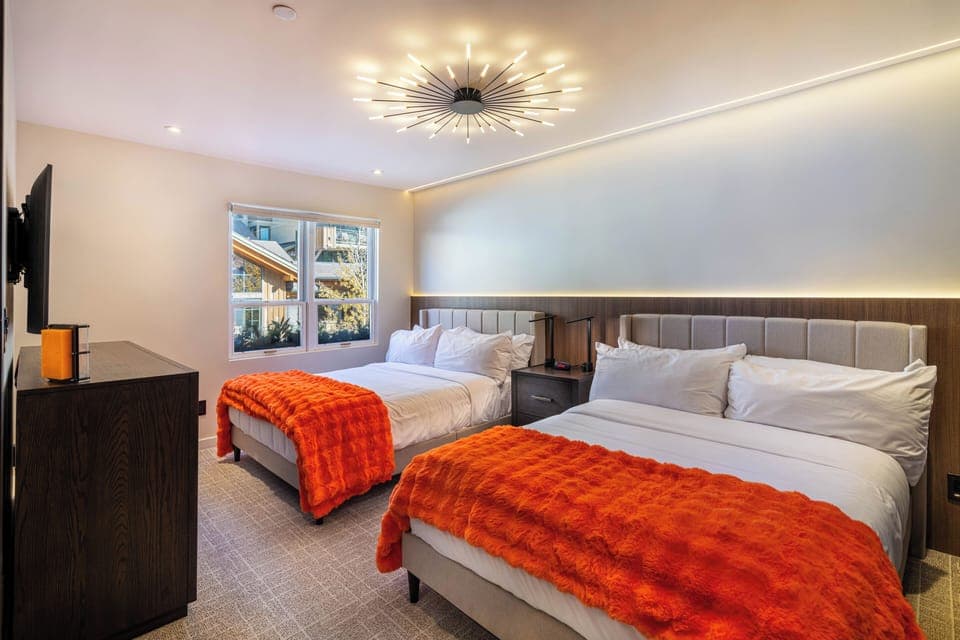 Drift into peaceful sleep in this stylish twin bedroom, where modern luxury meets cozy comfort with plush orange throws and stunning light fixtures.
