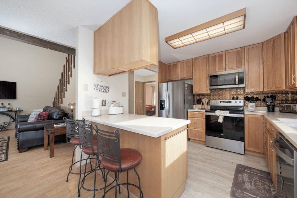 Your open-concept kitchen at 874 Kinnikinnick Road flows beautifully into the living area, featuring warm wood cabinetry, granite countertops, and stainless steel appliances for memorable meal preparation.