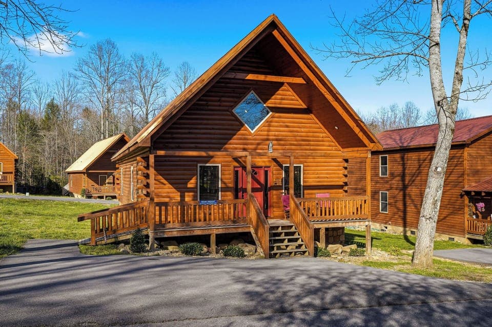 A charming log cabin featuring rustic wood construction with a distinctive diamond window accent and welcoming front deck.