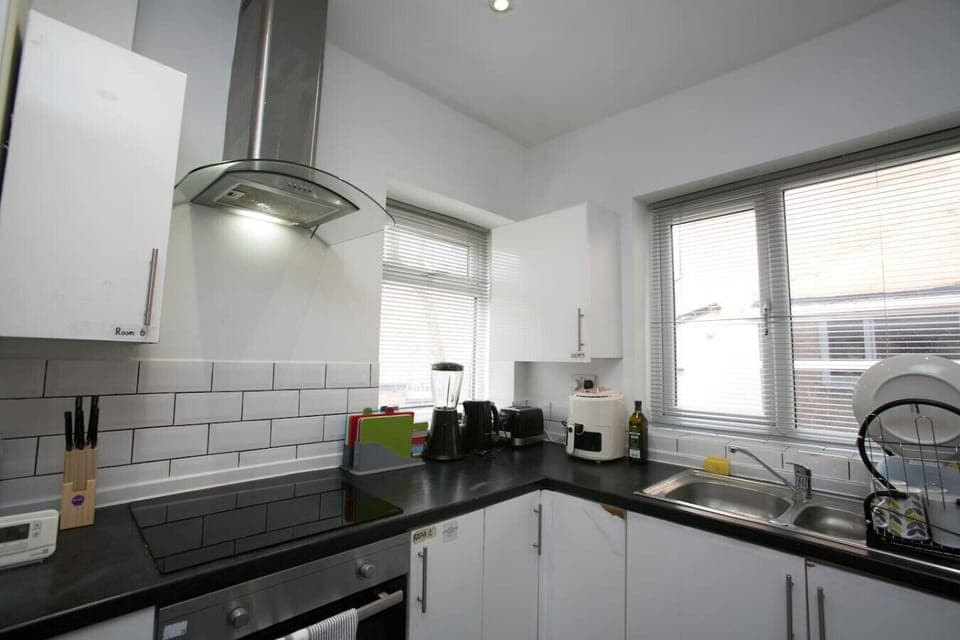 A kitchen corner with hob, extractor hood, and worktop appliances by the windows.