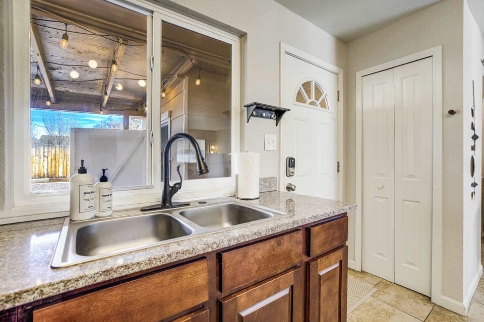A deep double-basin sink sits beneath a large window that fills the kitchen with natural light. The adjacent door provides quick access to the side yard and carport for easy unloading of groceries.