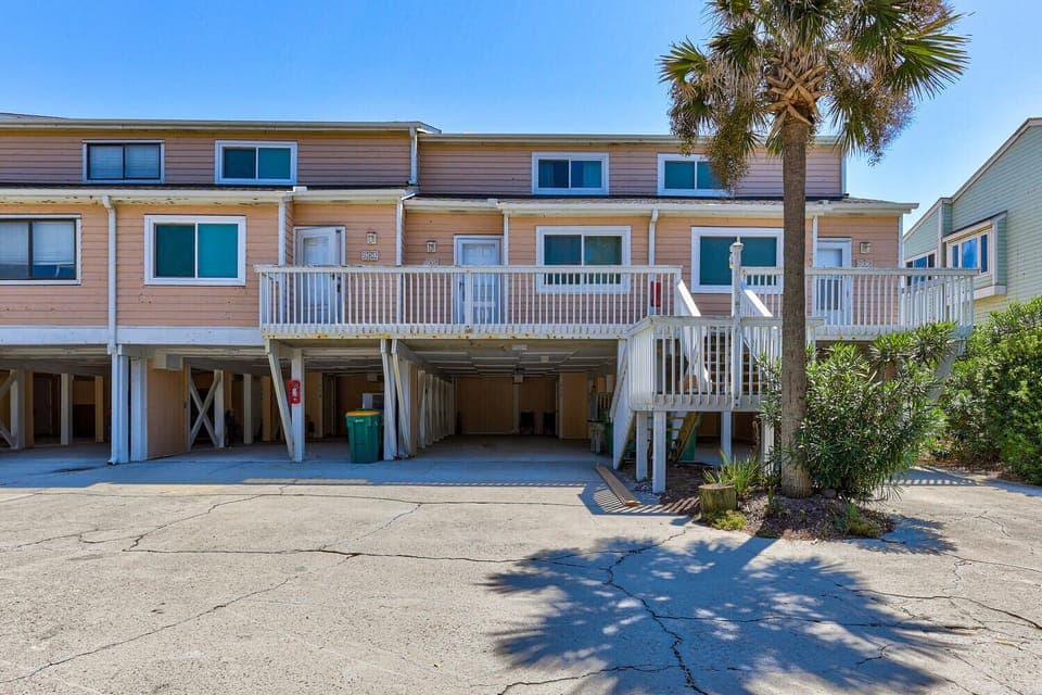 Beachside townhome with tropical palms, elevated deck, and covered parking in a quiet coastal community.