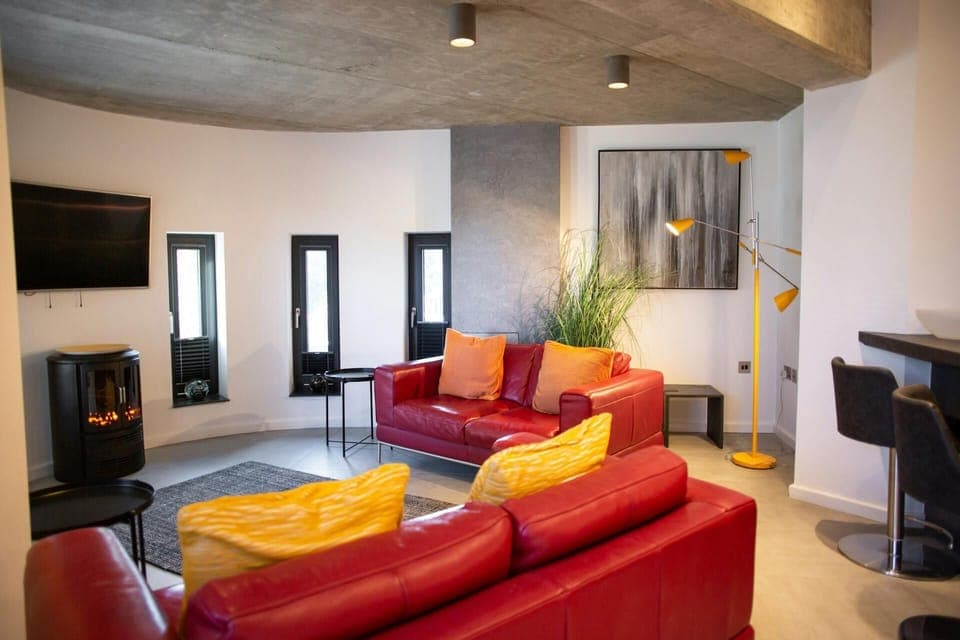 Living area with sofas, log burner, curved wall with long windows