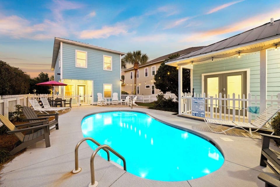 Charming coastal property featuring a private pool surrounded by comfortable lounge chairs and tropical landscaping at twilight.