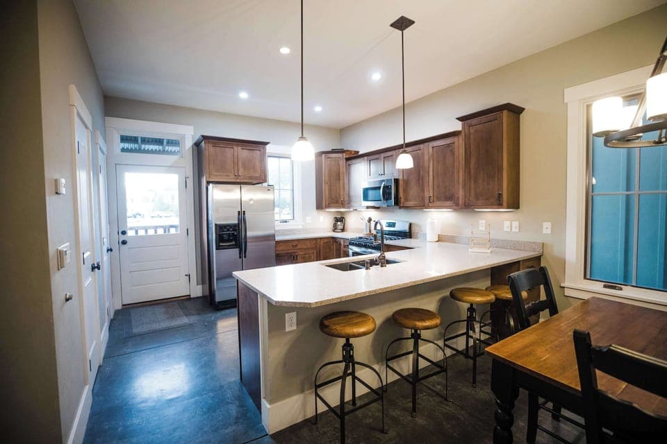 The kitchen features an oversized island with bar seating, warm wood cabinetry, pendant lighting, and professional-grade appliances, perfectly positioned within the open main-level layout.
